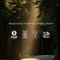 Sunlight streams through tall forest trees onto a winding road. Text reads Responsibly made for a happy planet above sustainability and women-owned business certification logos.
