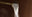 A brass measuring spoon pours a stream of white granulated sugar against a dark brown background.