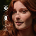 A woman with long red hair stands in sunlight with leaf shadows on her face. Three icons and text on the left read: Skin, Hair and Nails, Focus and Cognition, and Gut Health.