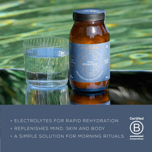 A glass of water and a jar labeled Ancient + Brave True Hydration sit on a green surface. Text below highlights electrolytes, mind and body benefits, and morning rituals. Certified B Corporation logo is shown.