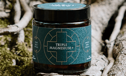 A dark jar labeled Triple Magnesium+ sits on a tree root outdoors, surrounded by moss and bark, promoting whole body health and daily ritual use.
