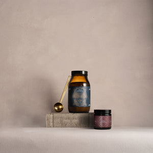 Two jars and a spoon on a gray surface with a beige background. Wild Collagen and Noble Collagen.