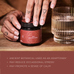 A tattooed hand holds a jar of Ancient + Brave True Ashwagandha beside a glass of water. Text below notes this adaptogenic herb’s ancient wisdom for stress reduction, calming effects, and balance restoration.