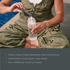 Person holding a water bottle with a label, sitting by a poolside.