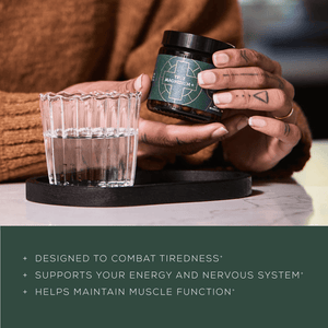 A person holding a jar labeled True Magnesium next to a glass of water on a black tray. Text below highlights benefits: combats tiredness, supports energy and nervous system, and helps muscle function.