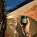 A person holds a jar labeled True Magnesium+ next to a glass of water and two white capsules on a golden tray by a pool. Text reads: Take 2 capsules daily, morning or night. Works well alongside True Ashwaganda+.