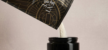 A bag labeled Ancient & Brave pours a white powdered supplement, likely collagen, into a black container against a neutral beige background.